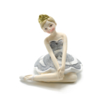 Kép 1/3 - Ezüst csillogó tütüben kecsesen ülő és a térdét megérintő balerina